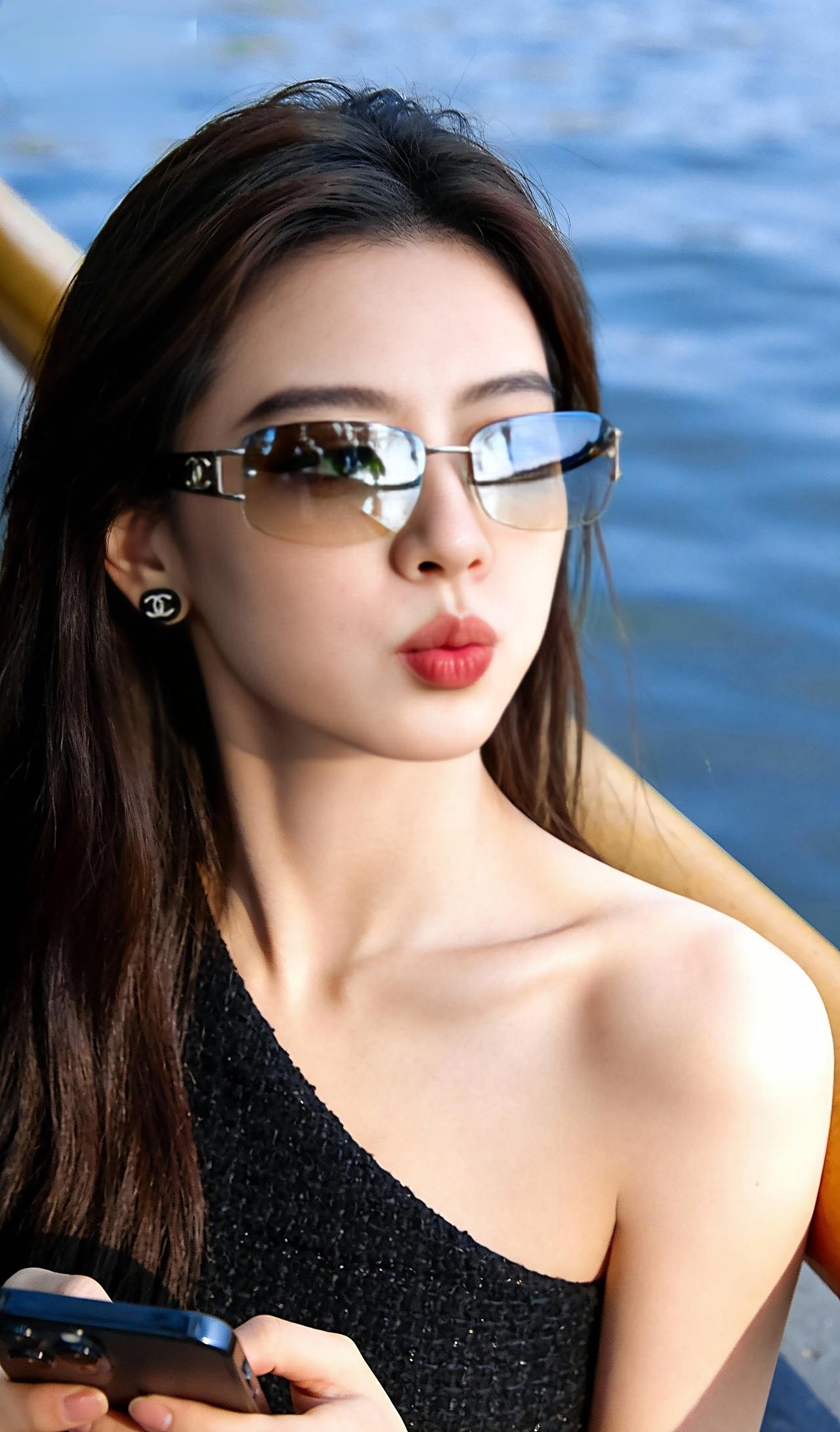 把夏日的温柔与热烈，都揉进水边的风里。镜片倒映着岸边的绿意，指尖轻握手机的模样，