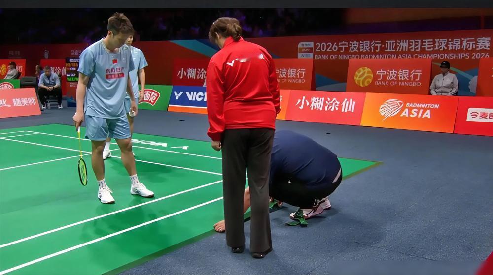地胶又在顶级赛事现场脱胶了。2026年亚锦赛男双1/8决赛前，工作人员跪在地上用