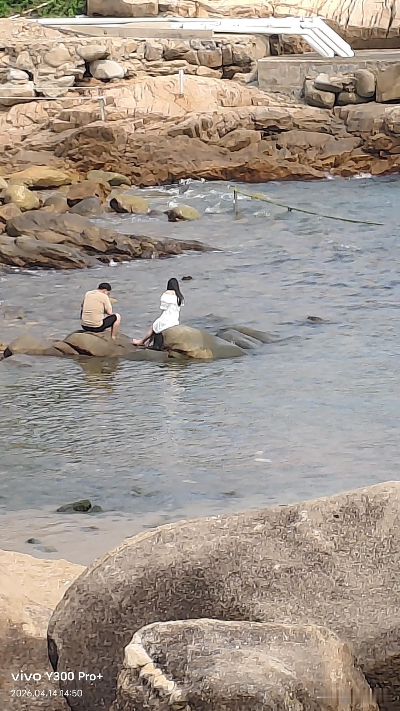 夏日炎炎，这对情侣坐在海边的石头上，周围是海水，真是会调情。