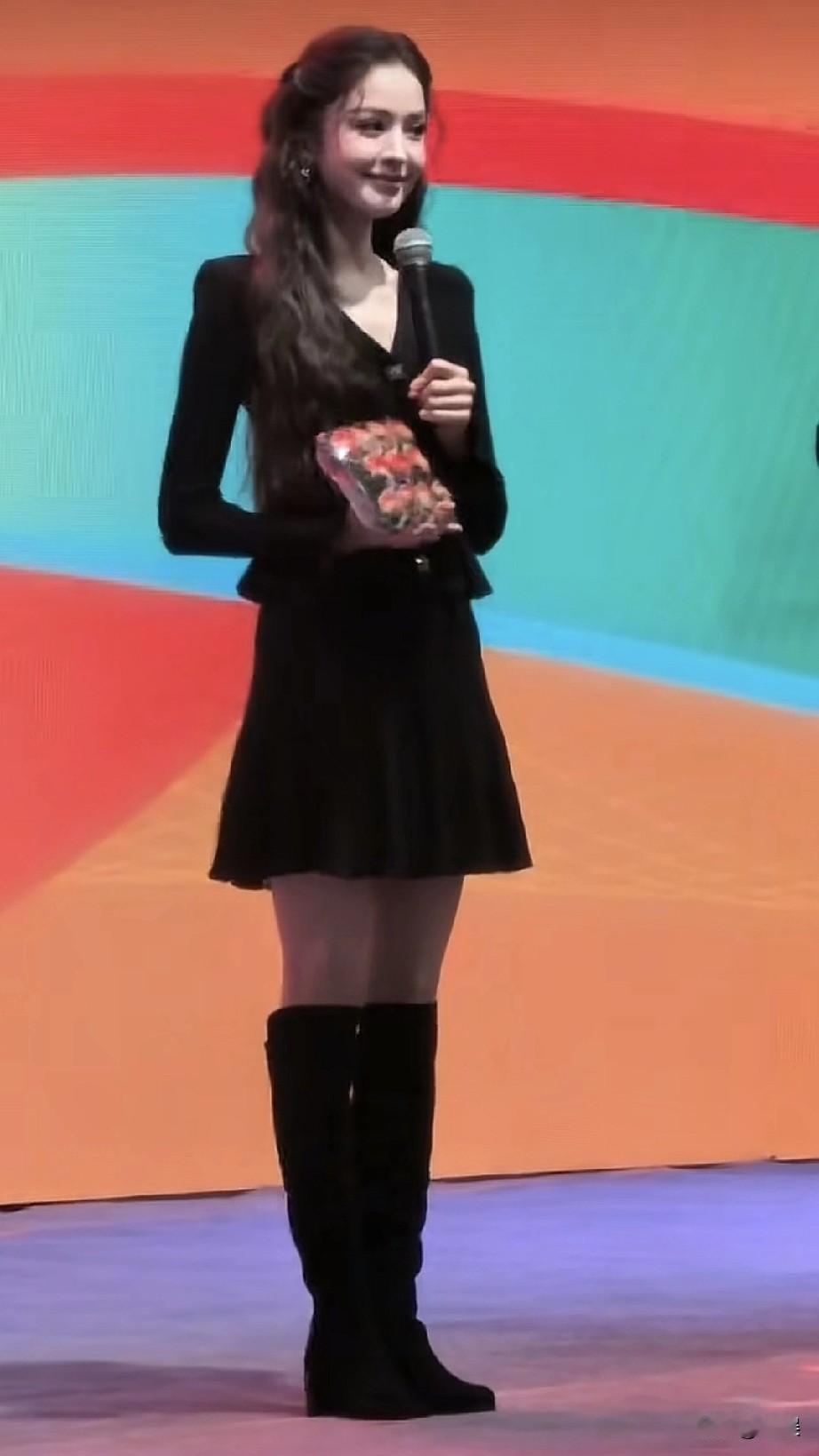 古力娜扎在活动现场，她一身黑裙搭配长靴，手持话筒