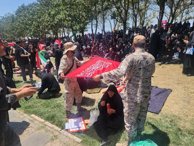 美伊以冲突 两名伊朗安全部队人员在伊朗殉难领袖的告别仪式上，为一名中暑的老年妇女