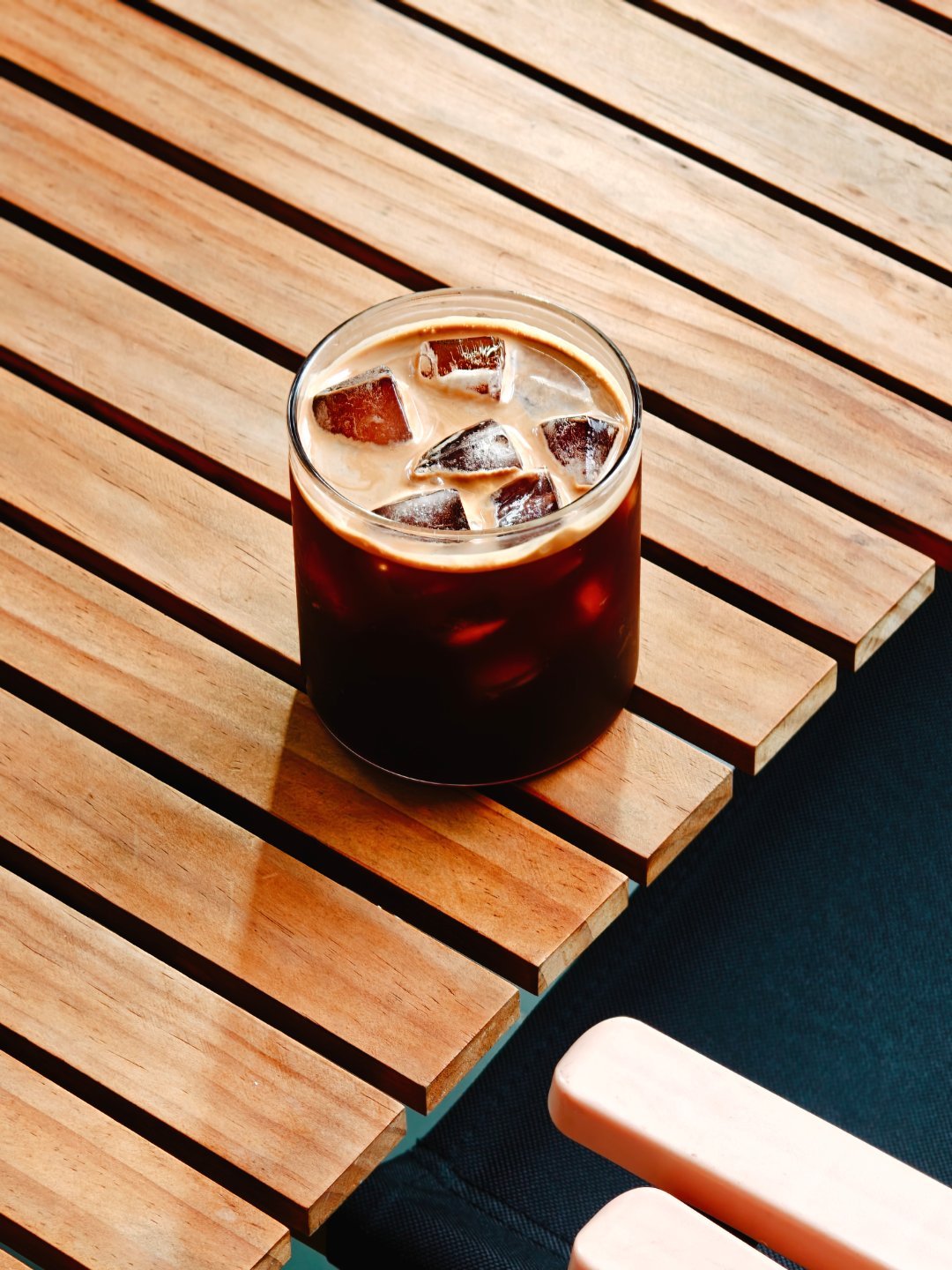 清晨的第一杯冰咖啡，冰块碰撞出清脆声响，棕色液体在杯中泛着光泽，小桌子带来自然气