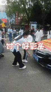参加高考的学生们，正在考场门口排队摸带有“985”的车牌，不过我却发现排队摸“9