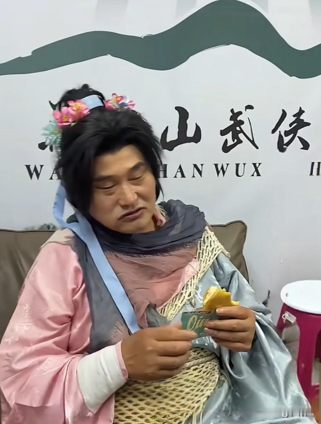 “大衣哥”朱之文古装扮相，休息间隙坐在后台吃铜锣烧。这身混搭古装造型十分搞笑，头