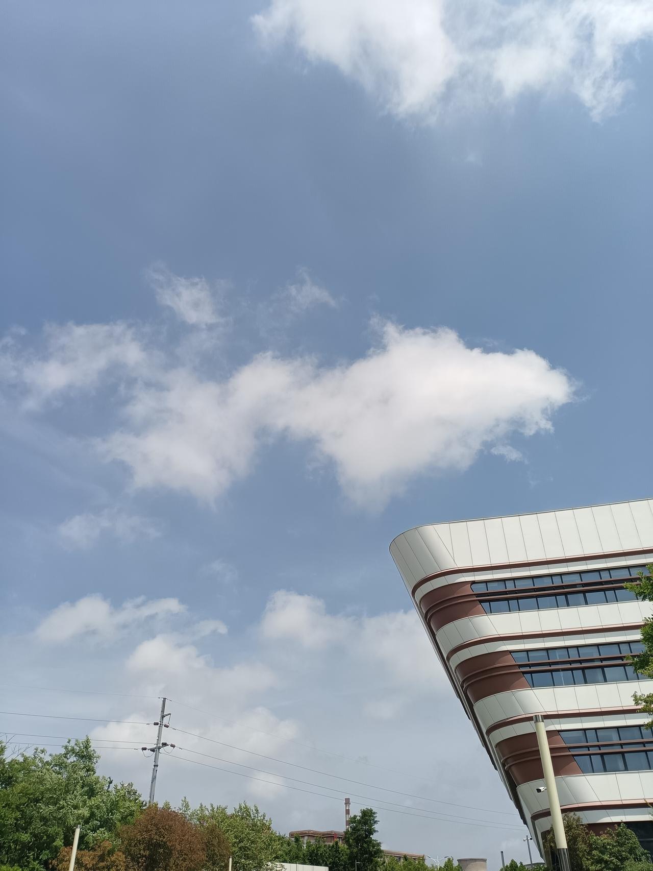 澄澈蓝天浮着蓬松云团，流线楼宇静立林间，清风衬出城市温柔清旷。