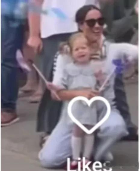 莉莉贝特公主模糊的正脸照，梅根单漆跪地，从背后搂着莉莉贝特，母女俩看起来还是很温