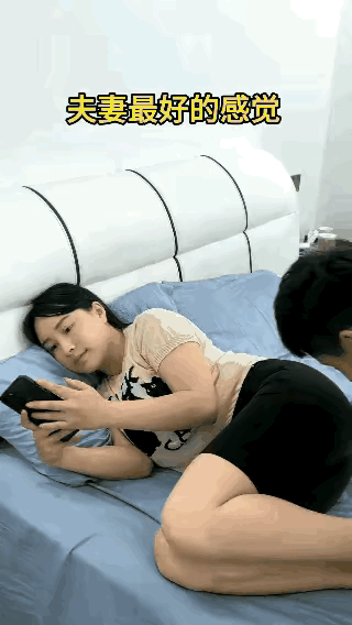 老婆下了班侧卧在床上看着手机，老公过来在她的脸部吻了一下，老婆高兴滴笑了起来，夫
