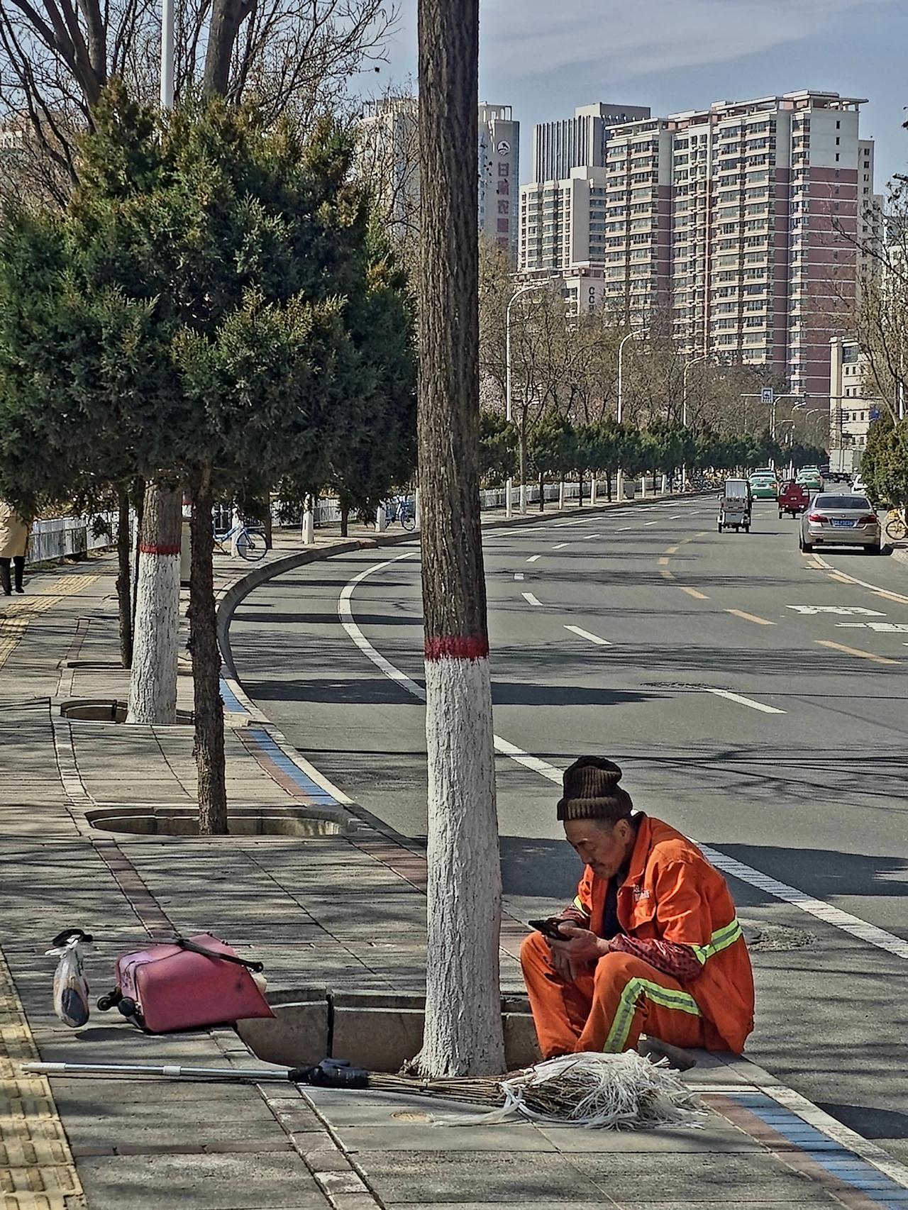 他坐在路边的树坑里，低头看着手机，把满心的情绪，都藏在这无声的凝望里。
当我的镜
