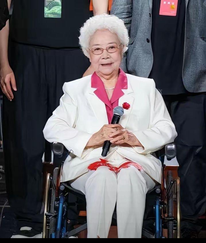 98岁的田华出席活动时坐在轮椅上，一身挺括的白西装搭配红色内搭，胸前别着红花，神