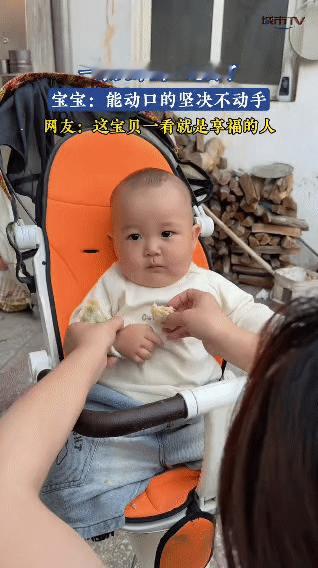 宝妈拿着食物凑近宝宝，宝宝乖乖坐在小座椅上，等着宝妈投喂，自己完全不动手去拿。就