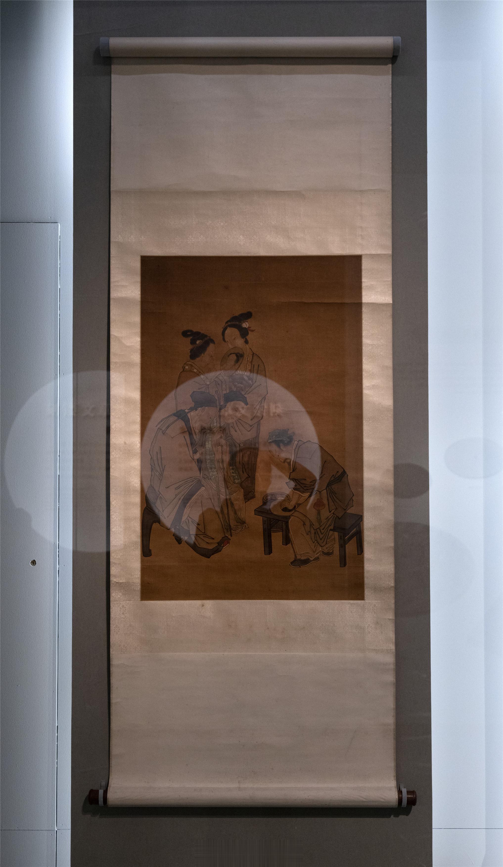 磨镜图轴清藏画面中磨镜匠人坐于木条凳后端，前端放镜，左脚踩绳以固定正在打磨铜镜，
