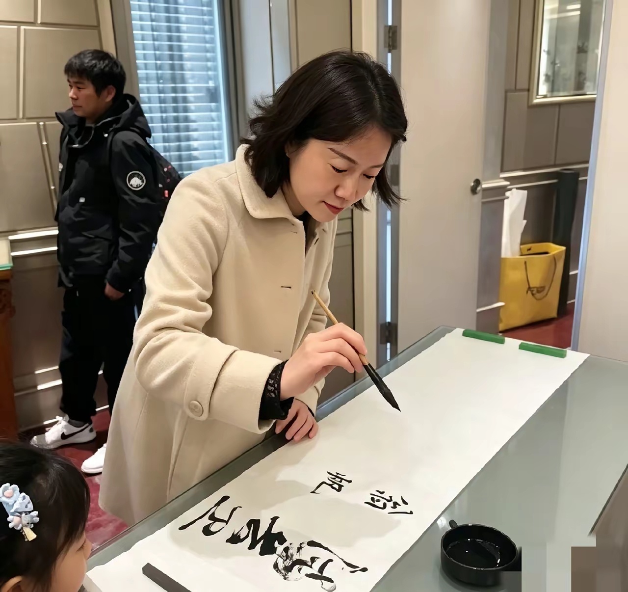 现场看翁帆写毛笔字，字迹清雅耐看。一旁的小女孩静静围观看得专注，她待人平和从容，