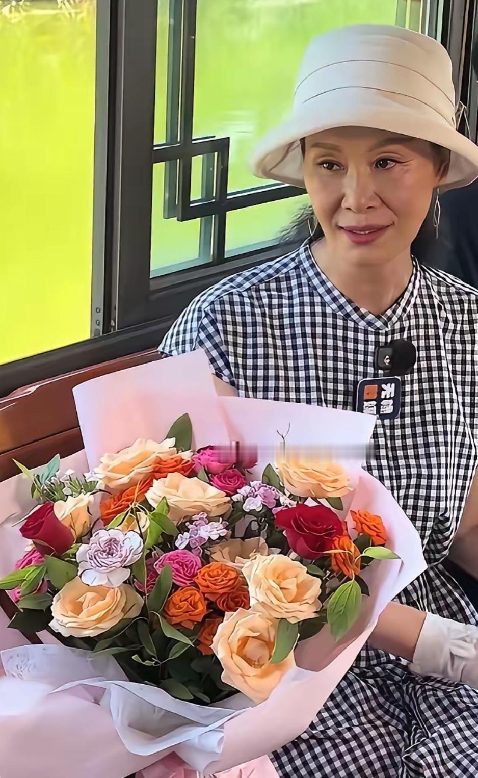 手捧花束，坐窗边微笑。这位女士是于老师吗？小时候经常听她的歌，美好的回忆。[作揖