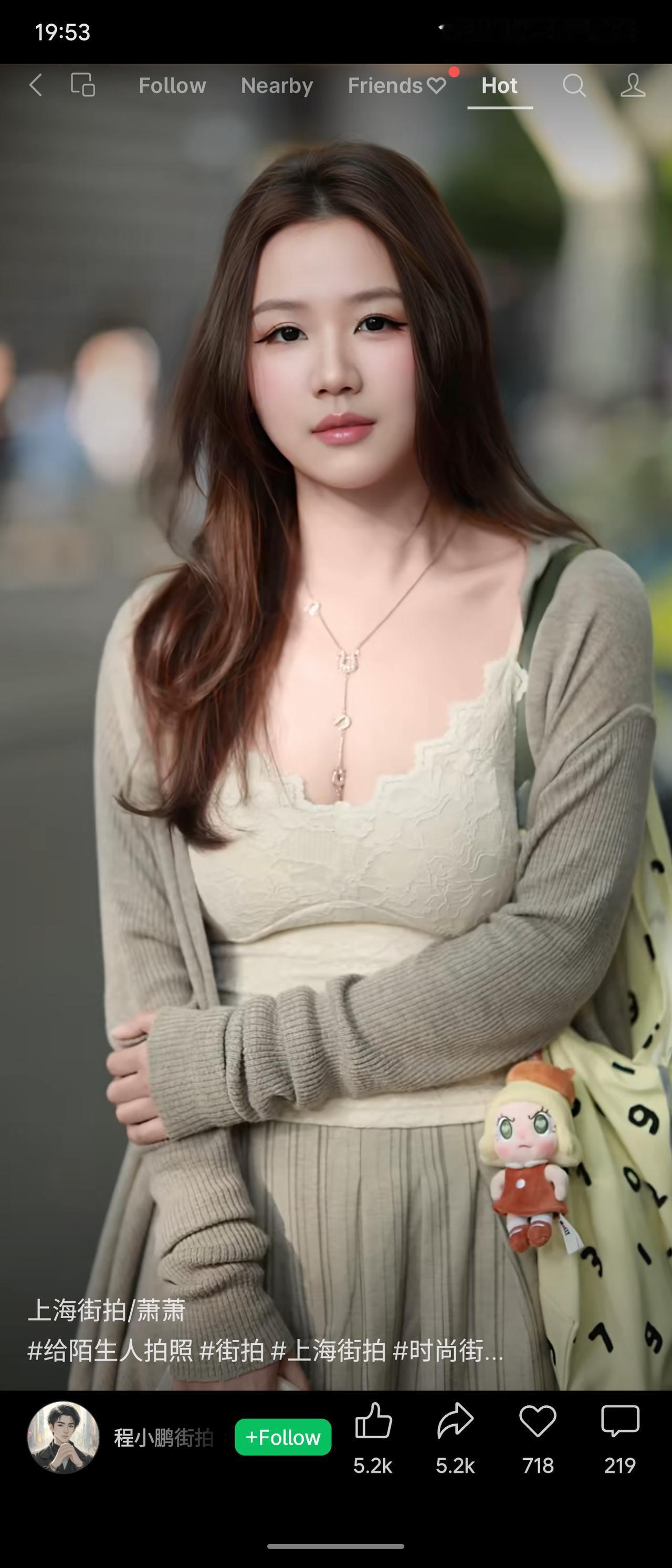 女生身着米白蕾丝吊带，外搭浅灰针织开衫，搭配同色系下装，温柔松弛，挎着带玩偶挂件