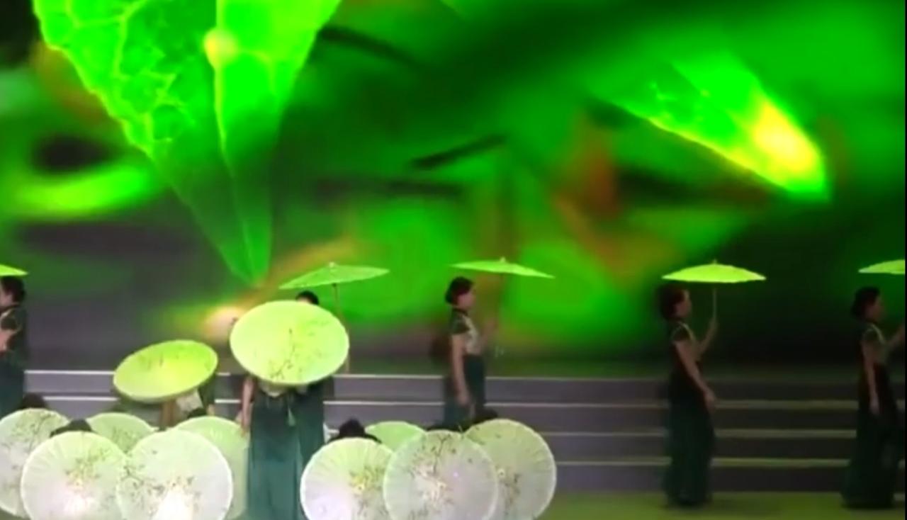 聚光灯下，李春虹带领的银发模特队手持油纸伞款款登台，翠绿舞美衬着她们优雅的步伐，