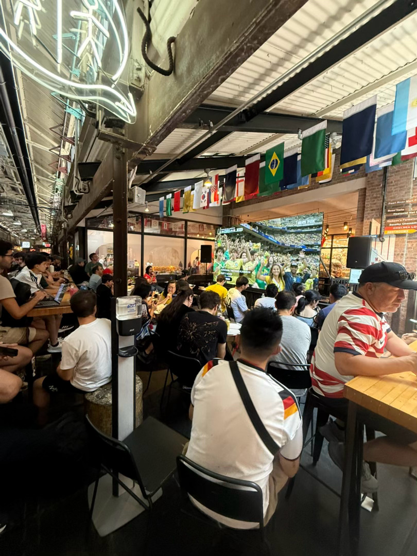 纽约Chelsea Market，人们坐在大屏幕前看巴西对日本，日本刚刚进了第一