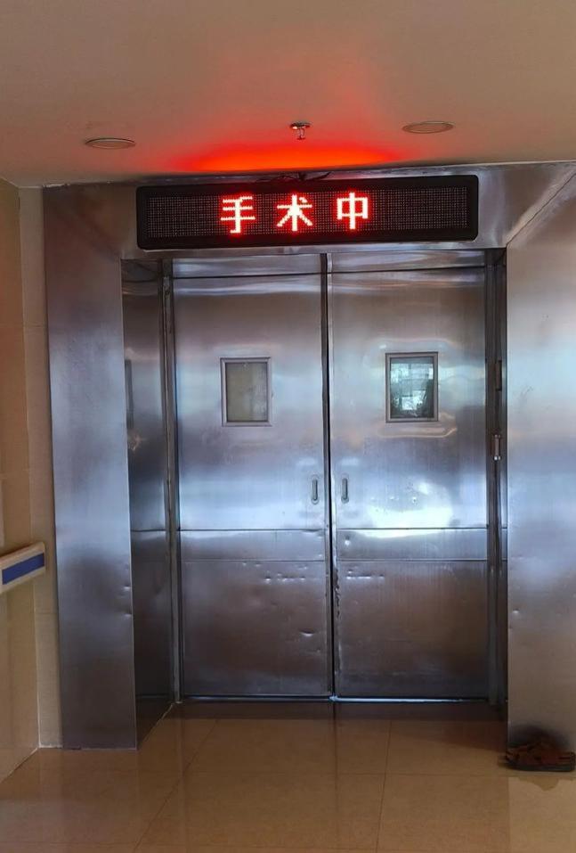 手术室外的椅子上坐着很多静静等待的家属，大部分人闭着眼睛，不时睁开眼睛望向手术室