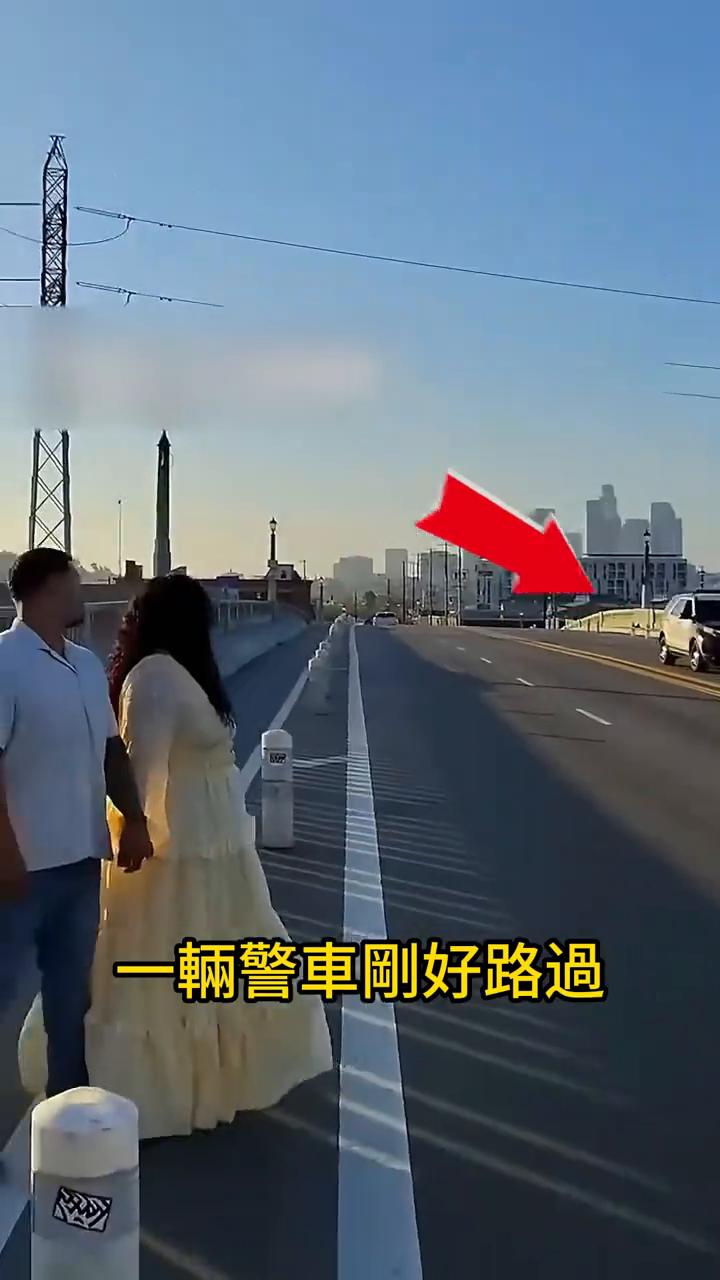 当这对情侣正在天桥上拍摄浪漫照片时，一辆警车刚好路过，并立马掉头开了回来。就在他