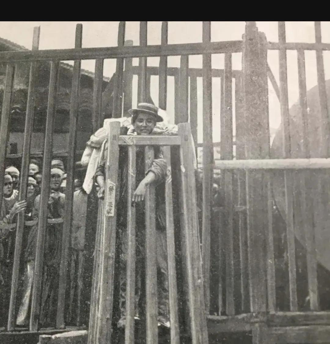 1905年，一名被囚禁在“站笼”的犯人，照片中的他戴着帽子，一脸微笑的看着镜头，