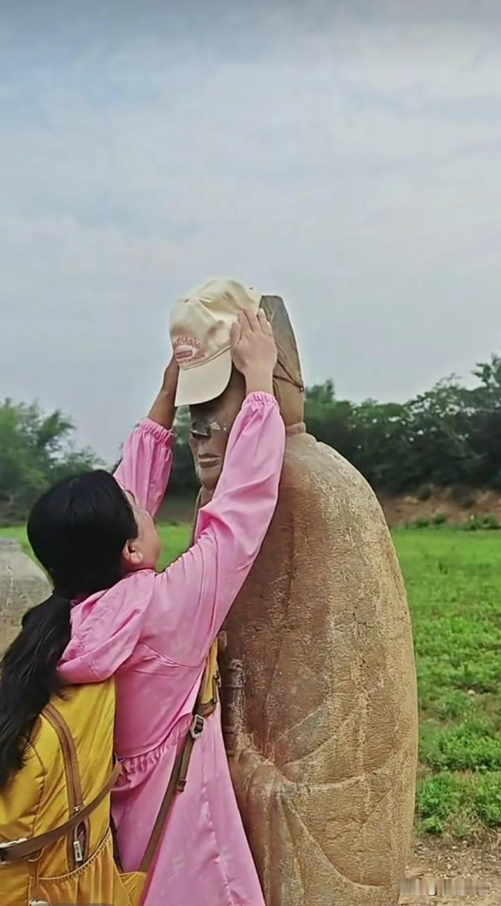 小姑娘非要给石像戴上帽子，她踮起脚才勉强够到，小心翼翼地将帽子戴了上去，随后双手