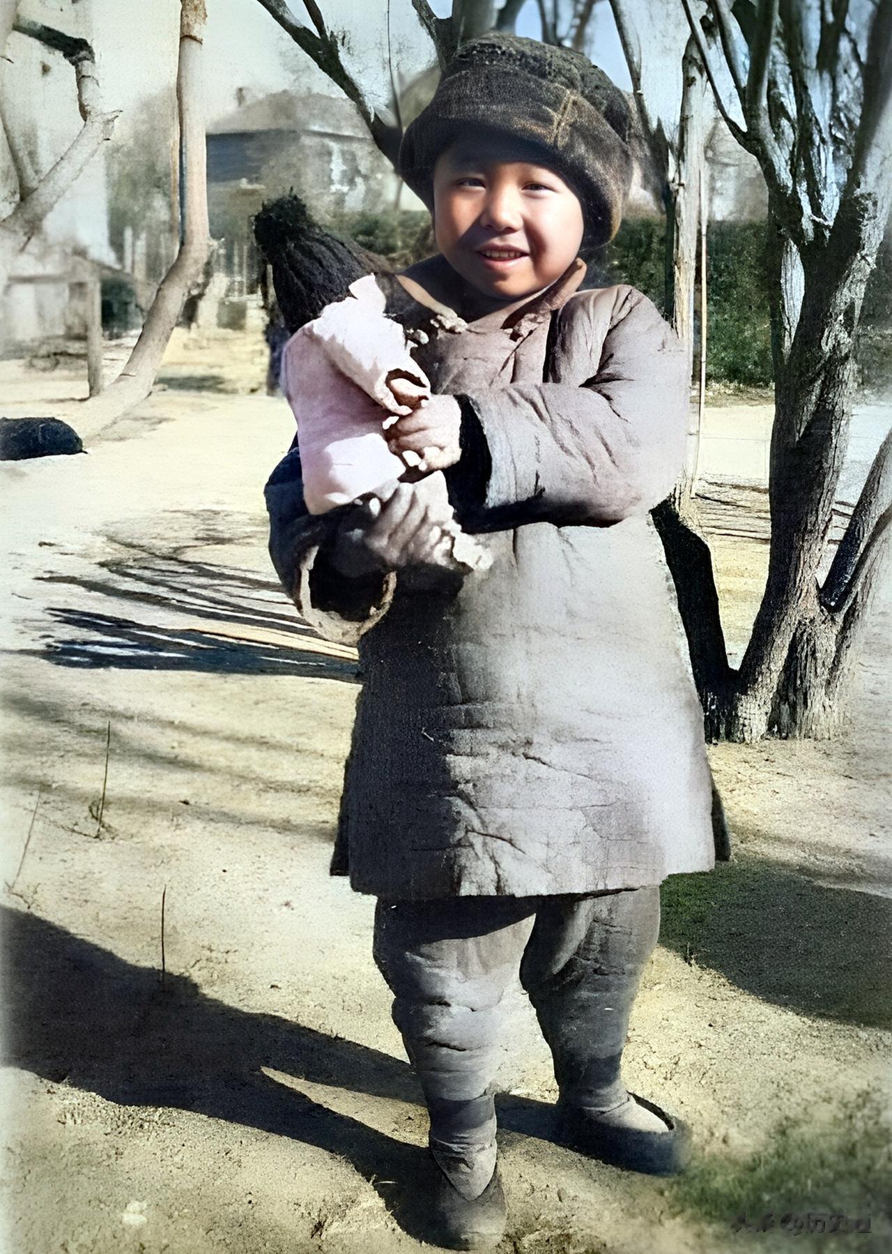 1930年，北平，小女孩拿着布娃娃在镜头前炫耀。寒冷的冬天，小女孩戴着棉帽，穿着