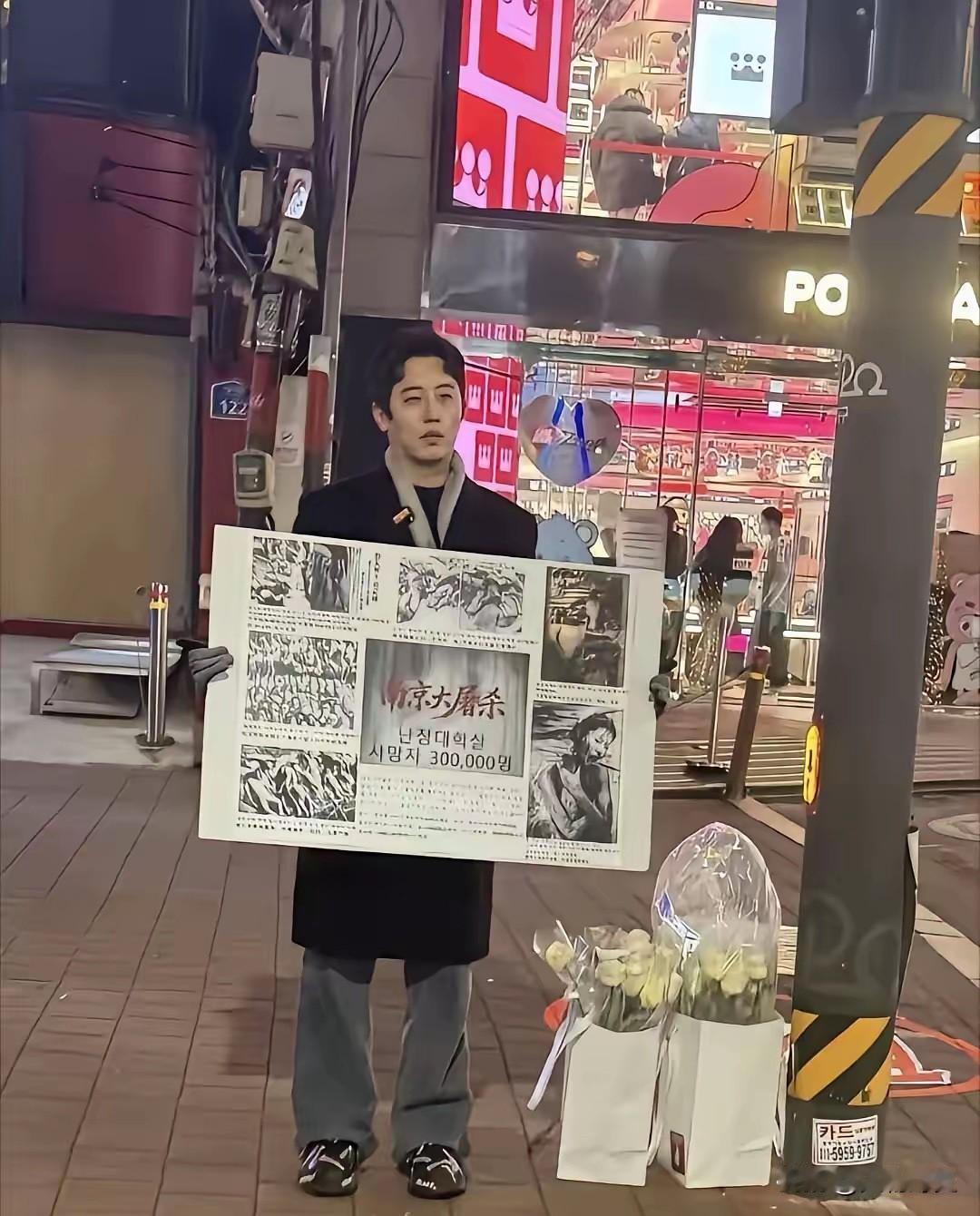 近日，韩国首尔的街头寒风刺骨，一名男子却身着单薄外套，手举海报静静伫立。他不顾凛