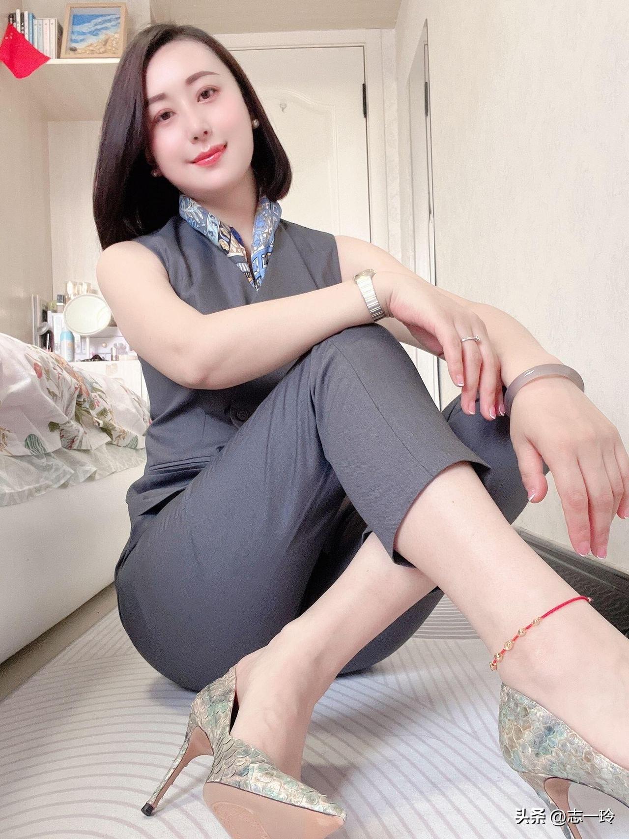 这位女士穿着一身灰色西装，坐在床上，脚搭在地板上，显得非常时尚和自信。
