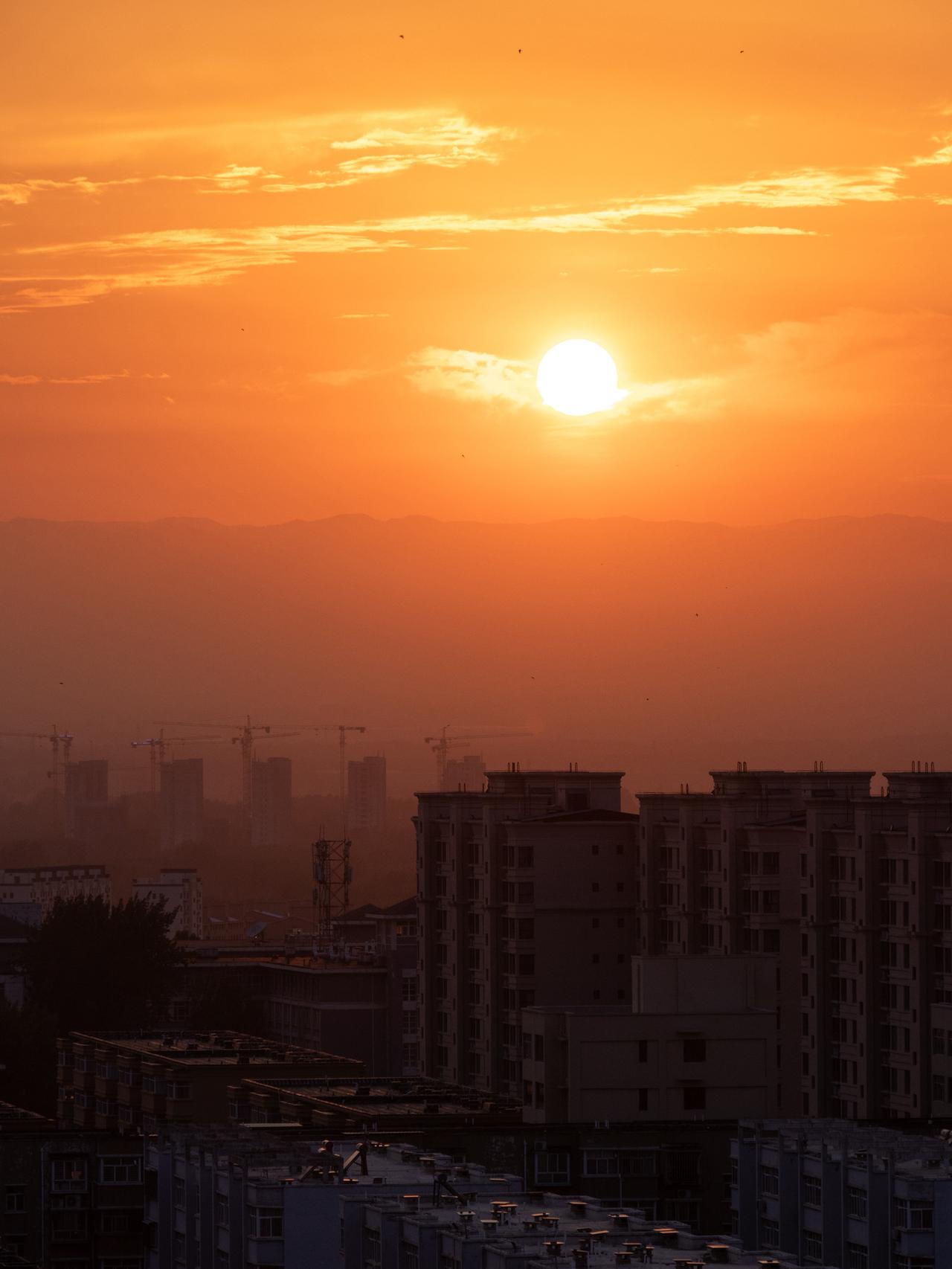 暮色漫过楼宇，夕阳悬在天际，或者说，当生活的痕迹、发展的印记（塔吊），都被夕阳温