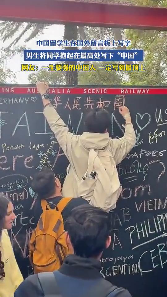 中国留学生在国外留言板上写字，男生将同学抱起在最高处写下