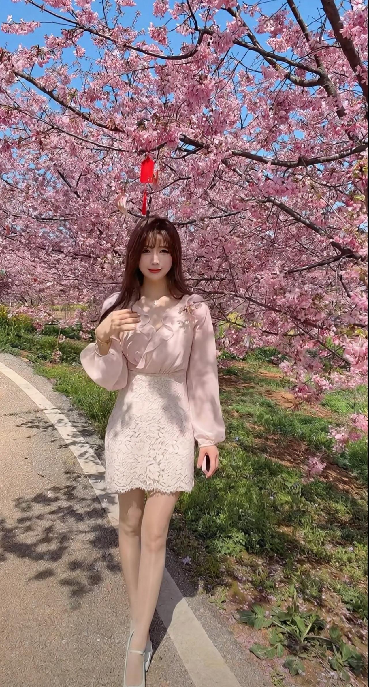 她留着温柔的棕长卷发与齐刘海，眉眼弯弯，妆容清透甜美，笑容明媚又灵动。身上穿着一