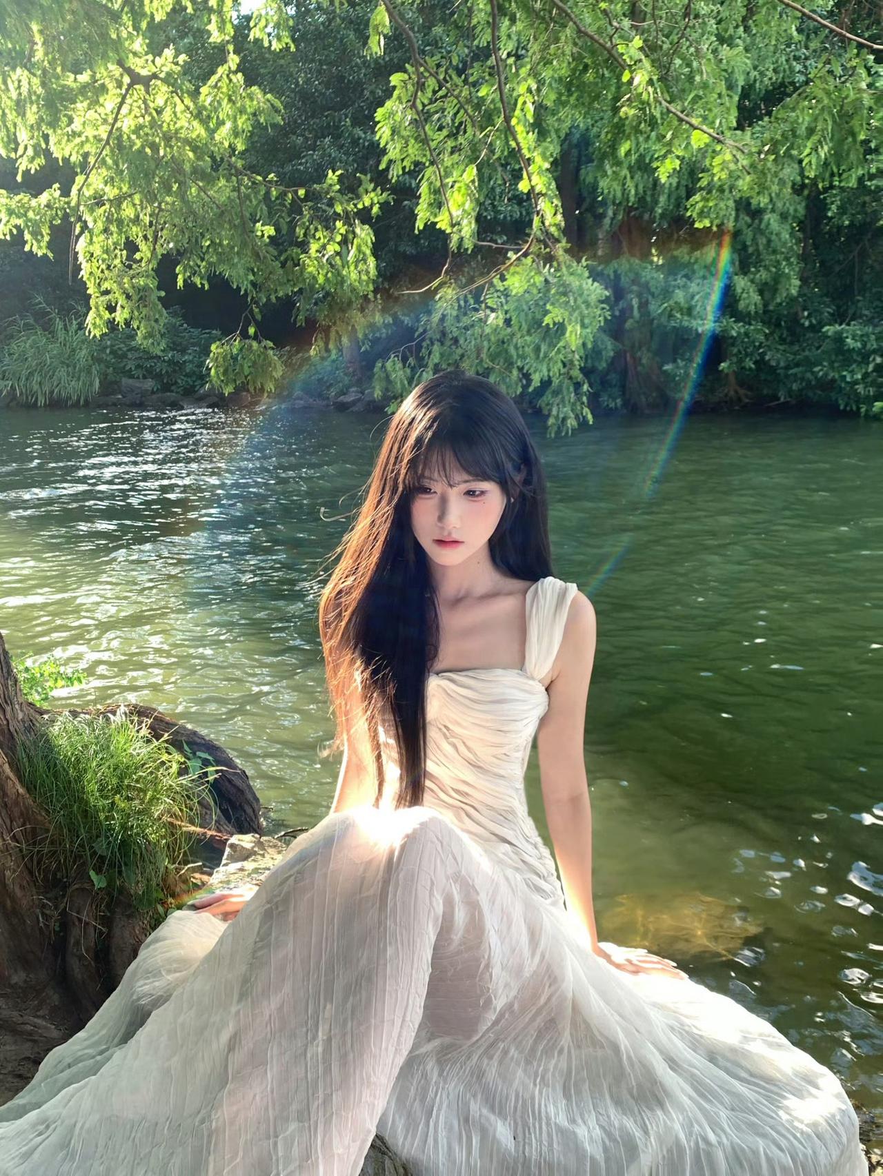 在绿意盎然的湖畔，她如仙子般静坐，裙摆轻拂水面，宛如梦境。