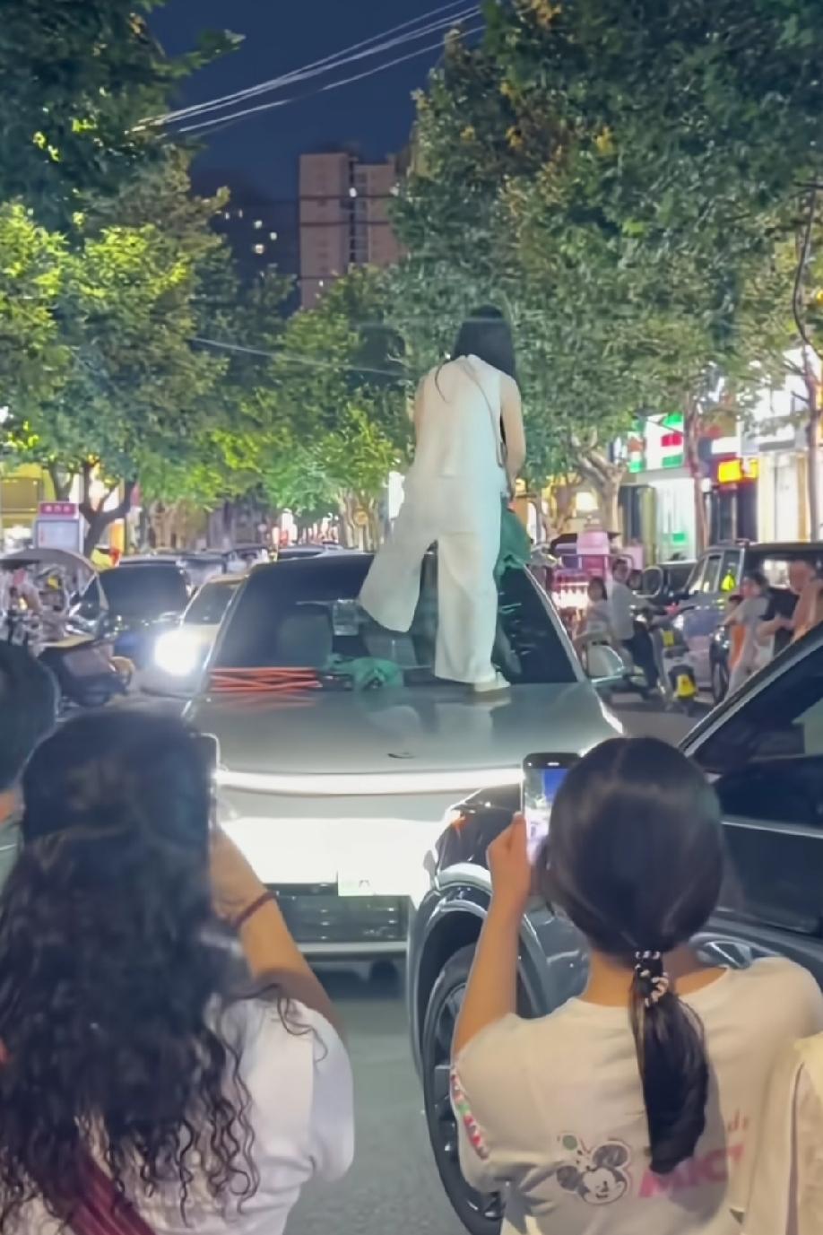 陕西商洛一闹市区，白衣女子当众砸着这台小汽车，车内有一年轻女子，在那里打着电话…