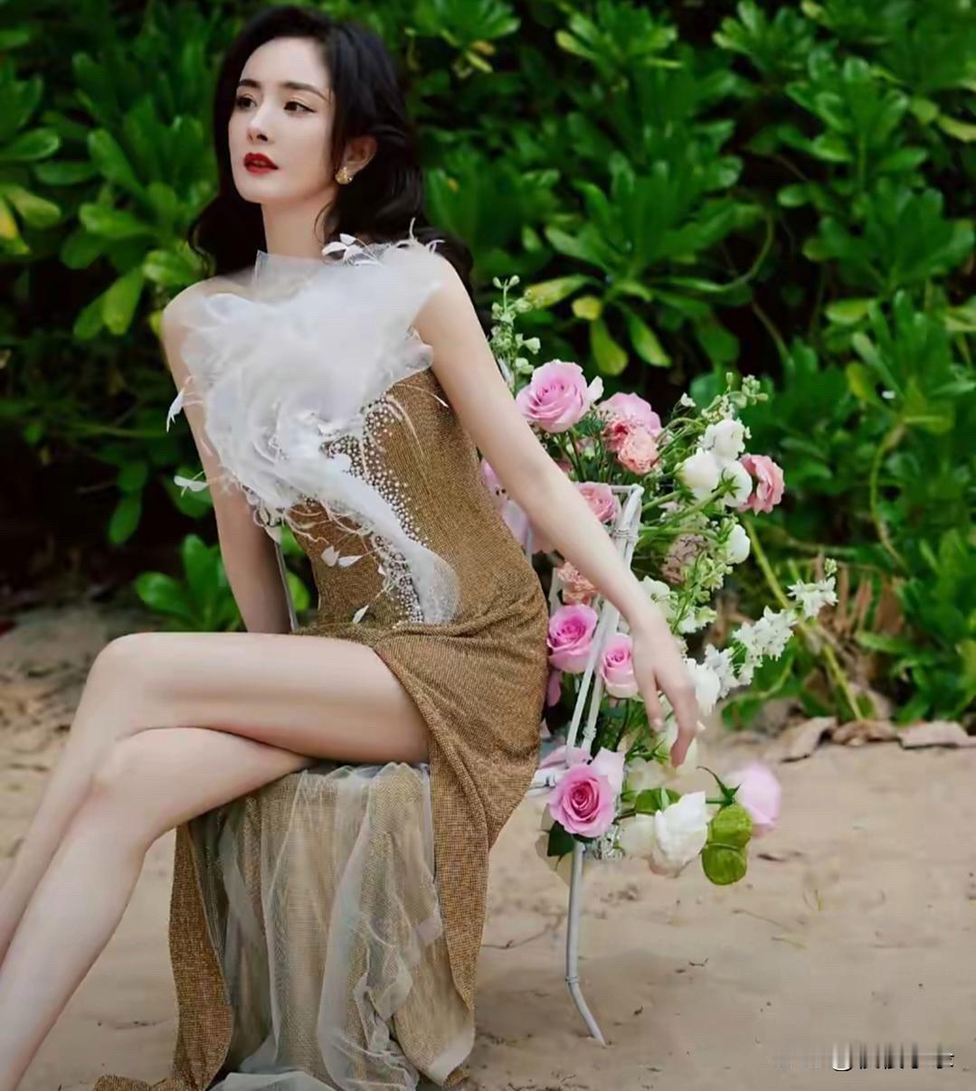 杨幂身着一袭金色开衩裙，在繁花绿植的映衬下美得宛如一幅精致画卷。闪耀的裙身与自然
