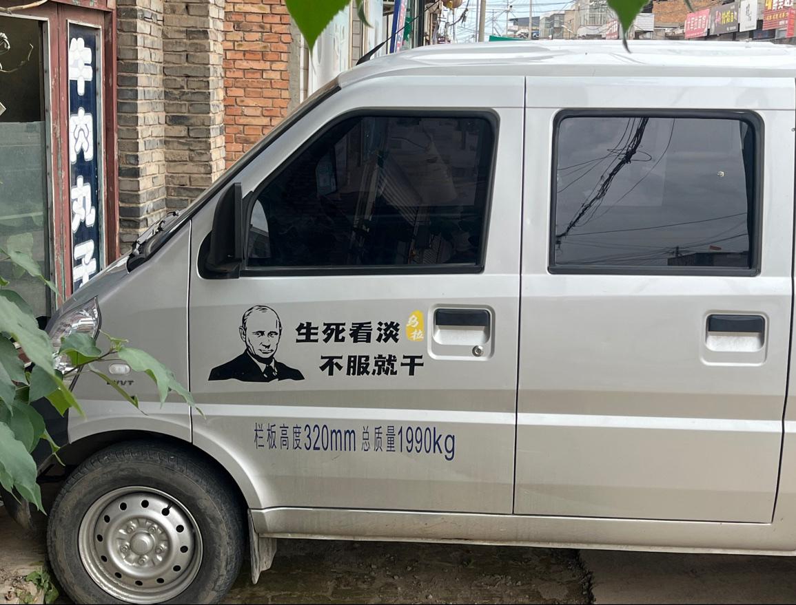 废弃店面门口停了一辆面包车，上面贴字是《生死看淡，不服就干》，还有《乌拉》二字，
