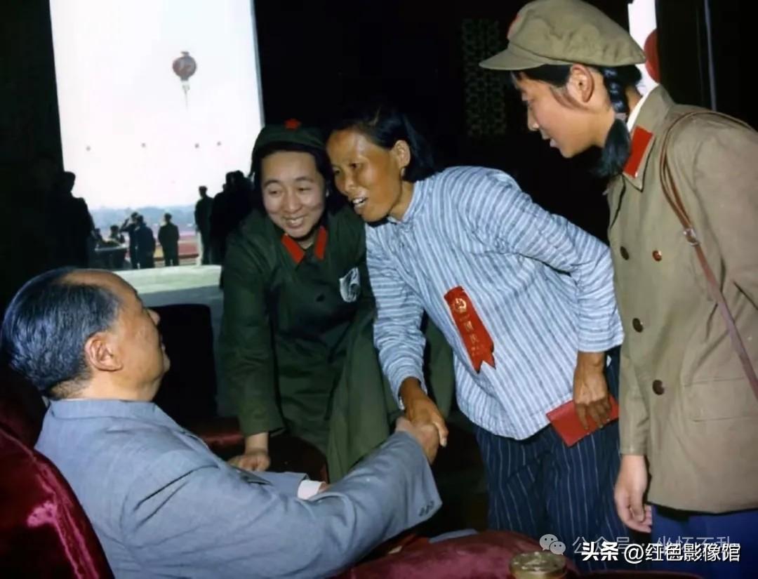 这张彩色历史照片拍摄于天安门城楼观礼活动期间：毛主席坐着与基层劳动模范/农民代表