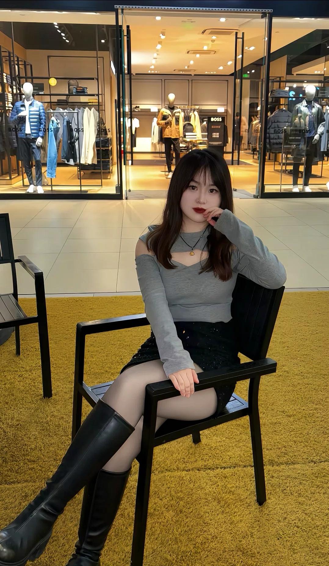 商场里的慵懒时刻，灰色挖肩上衣搭亮片黑裙，灰丝长靴揉出甜酷氛围感，在暖黄的地毯旁