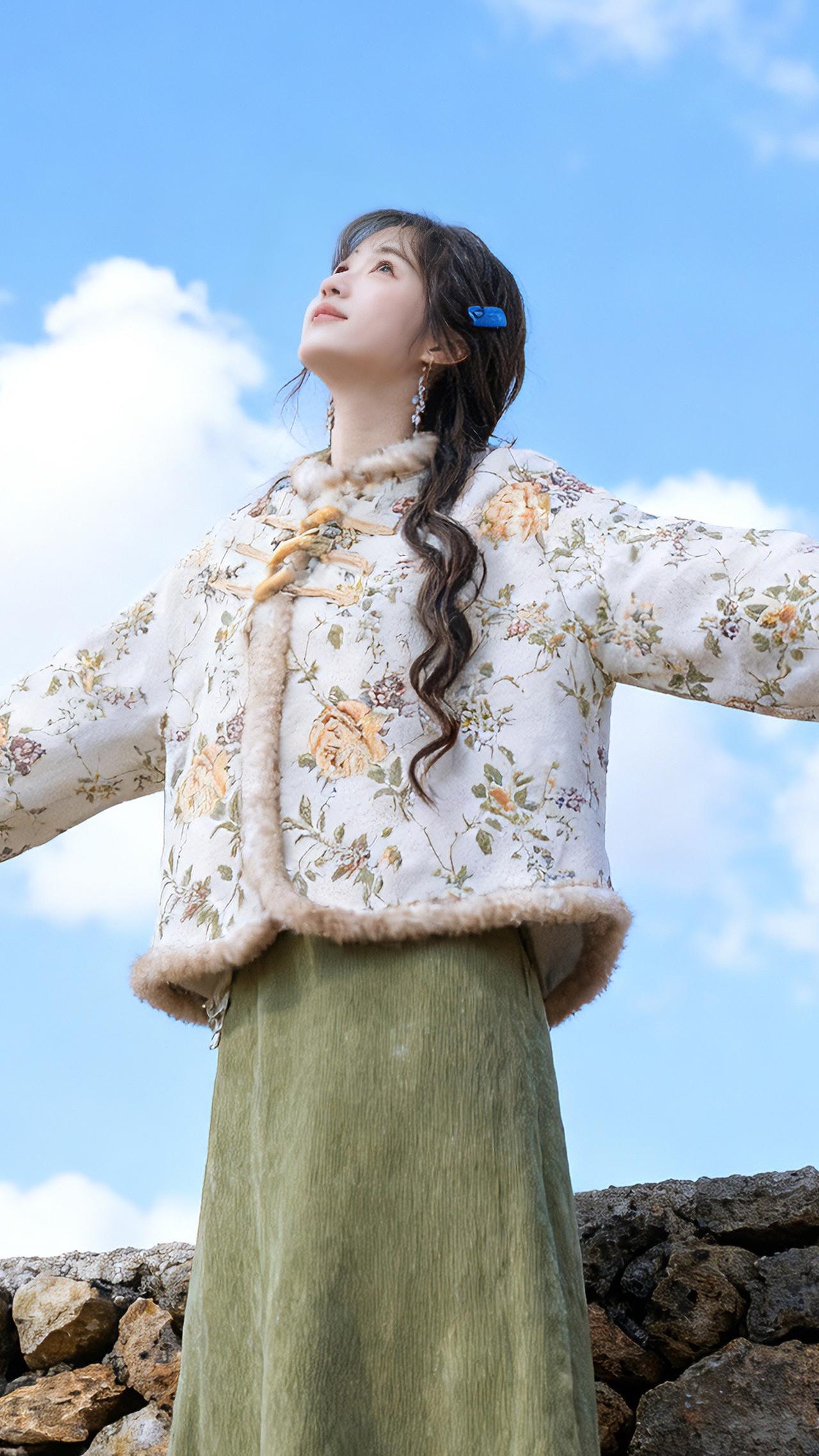 一个年轻亚裔女孩，黑色长卷发，戴着蓝色发夹，穿着照片同款衣服，坐在岩石堆上，黑色