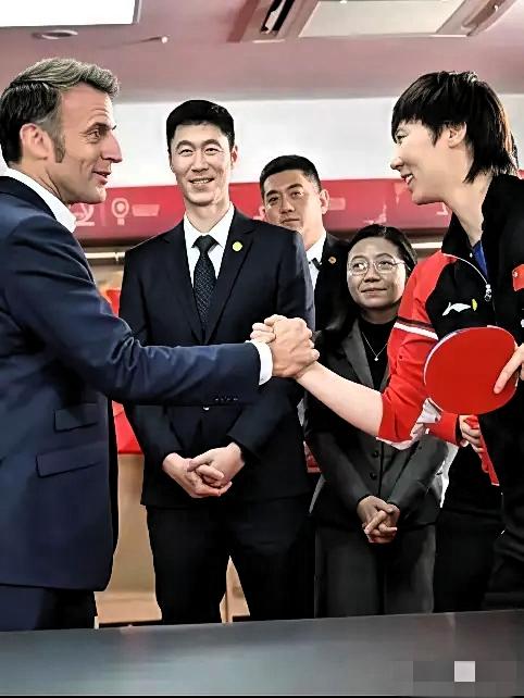 马克龙紧握王曼玉的手笑道：乒乓球打不过你，但扳手腕是我的强项，肯定能赢！王曼玉笑