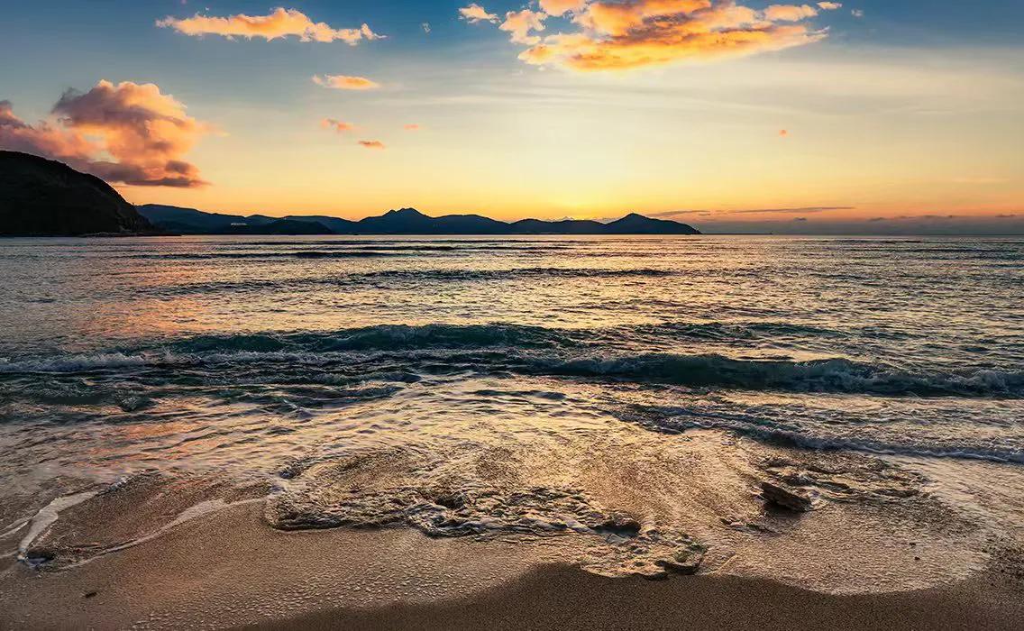 夕阳下的海岸线，温柔的海浪轻拍，静谧而美丽。
落日照海域 落日下的海面上 在海边