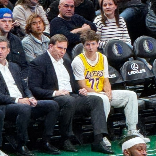 雄鹿客场险胜独行侠，比赛中一位身穿东契奇湖人球衣的男孩坐在独行侠老板的身边，独行