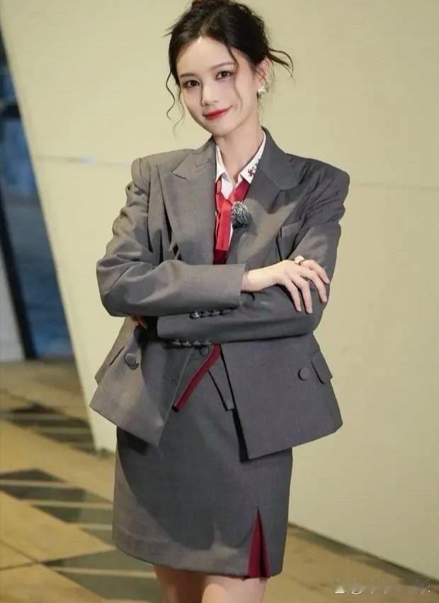 李一桐身穿灰色制服，配红领带美丽迷人 ，抱着双臂微笑甜美可爱。 