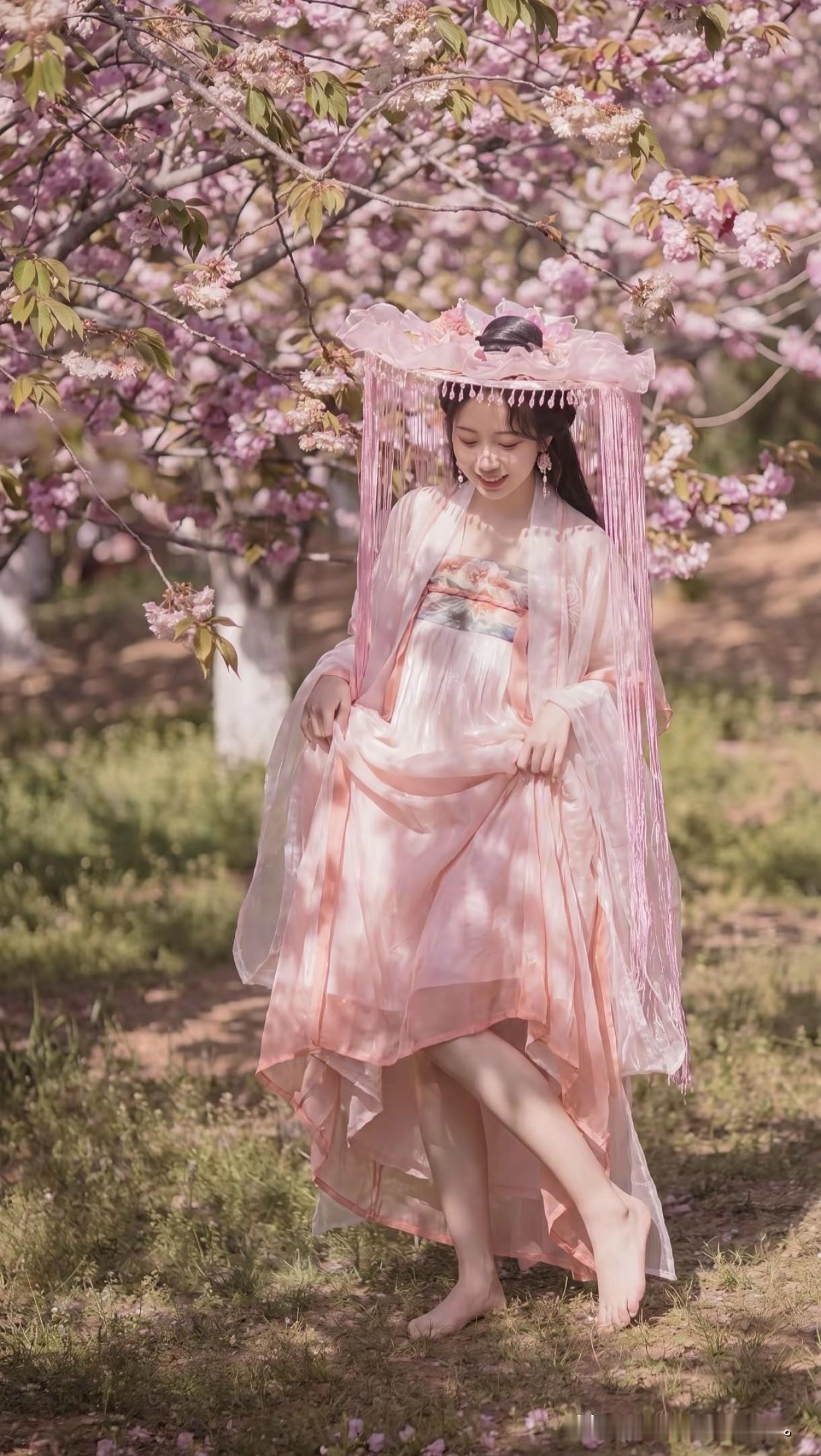 一袭淡粉汉服，头戴流苏花帽，
像是从唐诗宋词里走出的才女。
身畔是漫天飞舞的樱花
