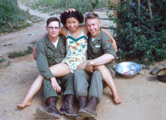 1947年，一名穿着清凉的韩国女子双腿叉开，以一种十分豪放的姿势坐在两名美国大兵