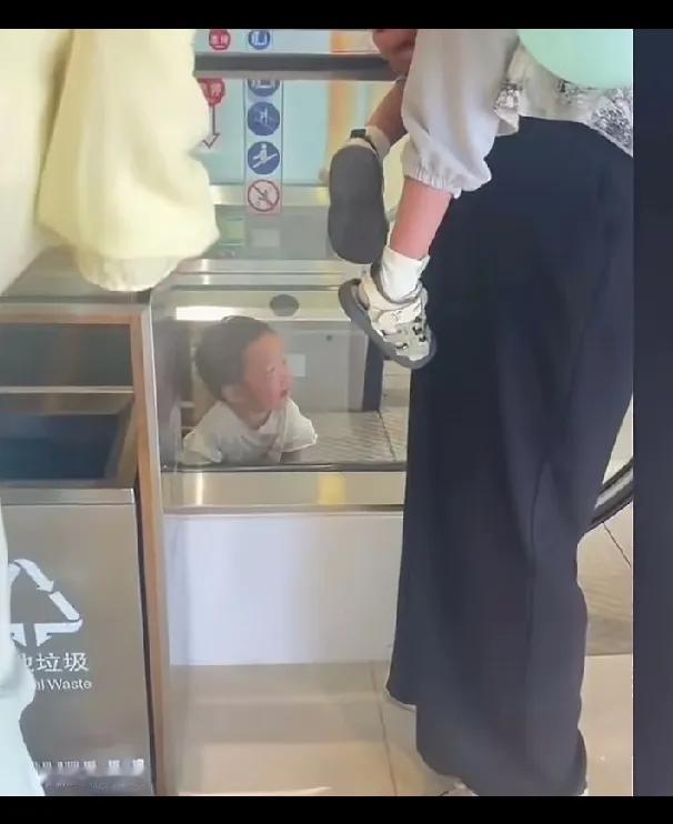 女子带着自己刚会走路的孩子，在电梯边上玩，开心的给小孩拍视频，路过的人一再提醒她