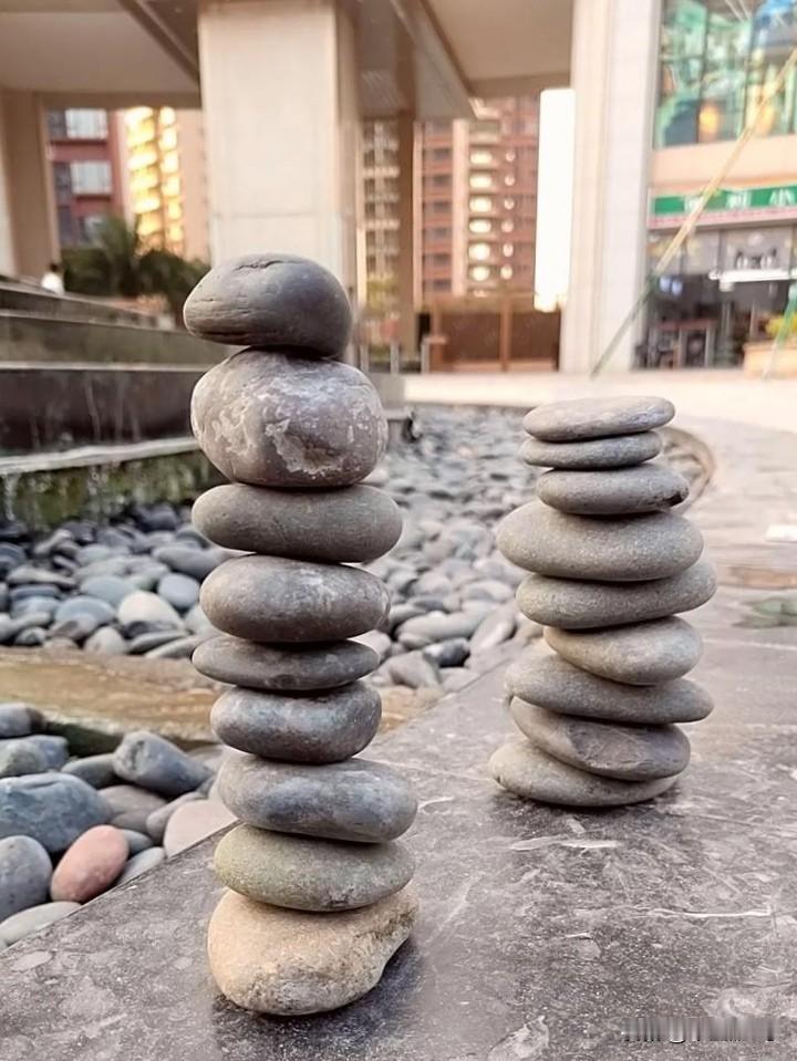 温馨的童年画面。
公园草丛边的小块空地，有大小薄厚好几块石头，从大至小摞起来，石