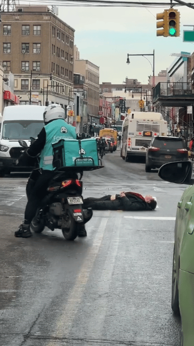 纽约街头一景，人行横道的路人和过路口的车从躺着的人身边过去，顶多也就是多看两眼。