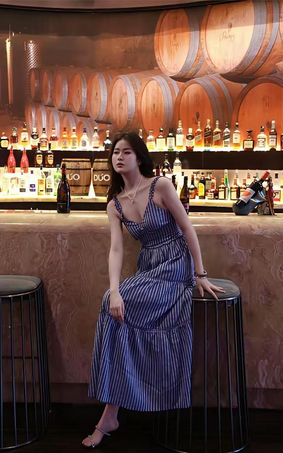一位女士坐在酒吧高脚凳上，背景是酒架。