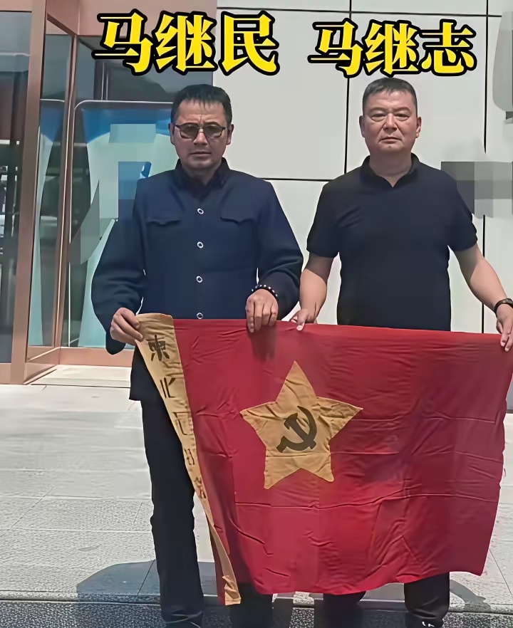 杨靖宇将军两位孙子，马继民和马继志两人共同手持一面带有“东北抗日联军”的旗帜，一