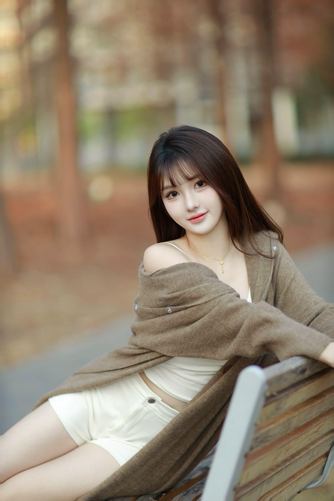 秋日暖阳下，少女倚靠长椅，温柔微笑，散发迷人魅力。