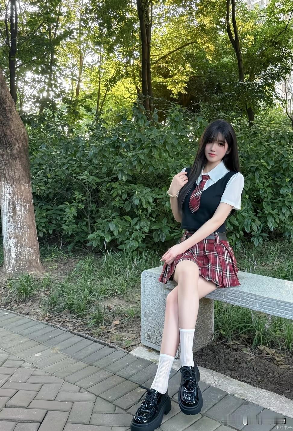 一个女孩坐在公园长椅上，穿着校服。